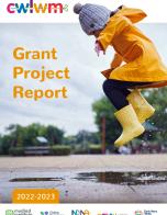 Child wearing bright yellow rain coat and grey hat with a bobble jumping in puddles