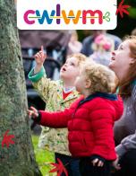 Children, one wearing a bright red coat, look up at the leaves from a tree