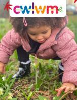 Girl wearing pink coat crouching to touch the grass