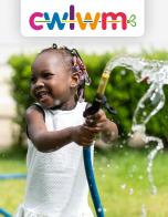 Girl with colourful beads in her hair smiling as she plays with a hose. Text reads: Newyddlen cwlwm – tymor y gwanwyn 2023